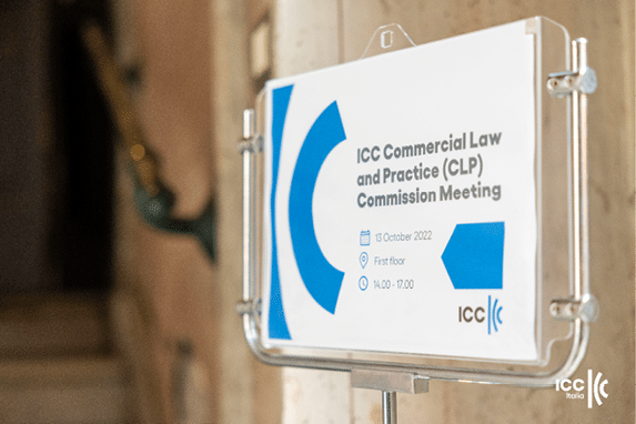 Placa em suporte met lico anuncia reuni o da Comiss o de Direito Comercial e Pr tica do ICC com data, local e hor rio em ambiente interno. Yapay zeka taraf ndan olu turulan a  klama