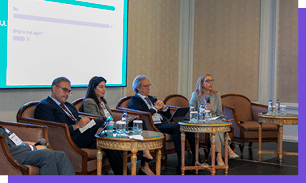 Cinco adultos sentados em cadeiras em um palco participam de um painel de discuss o com um tel o ao fundo exibindo uma enquete interativa. Yapay zeka taraf ndan olu turulan a  klama